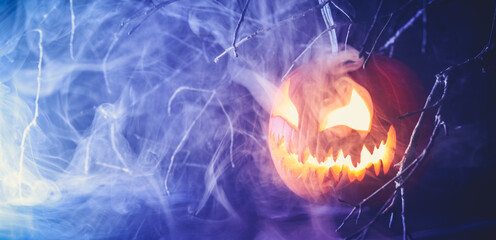 Spooky Halloween jack o lantern pumpkin with carved scary face glowing and billowing smoke in the night. © Leigh Prather