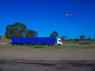 Truck on a freeway with plane flying overhead in Australian Country Town midway between Sydney and Melbourne with nice blue sky and lush green trees as a backdrop