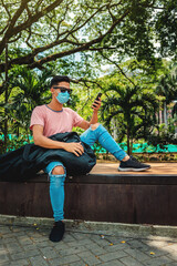 Fototapeta premium A handsome young man sitting, going to work, using his mobile phone, selfie, wearing a protective mask over his face
