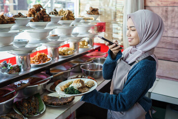 portrait of young muslim woman take photos of traditional food by phone