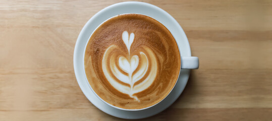 Top view of white cup of hot coffee latte art milk foam heart shape wooden table with copy space.