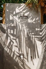 Outdoor shower in garden of luxury pool villa, shadow from palm trees on grey wall
