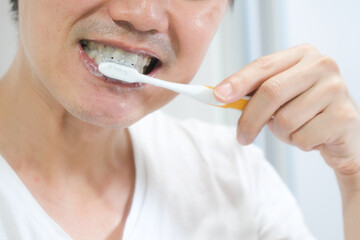A young Asian man, he cleans his teeth with a brush and toothpaste.