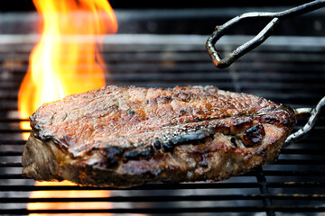 Grilled steak meat on the grill of the grill that has a flame