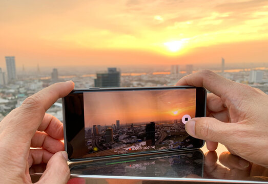 Young people take pictures of the buildings in the city. Sunrise time He uses a high-angle recording photo phone.Travel concepts and technology