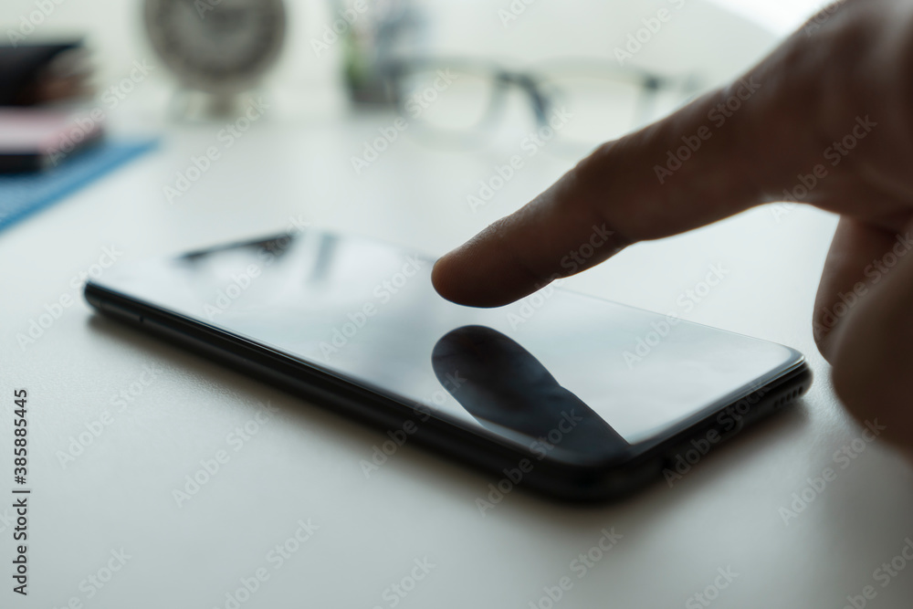 Poster close-up of a man using a smartphone with his finger touching the screen with warm light tones.
