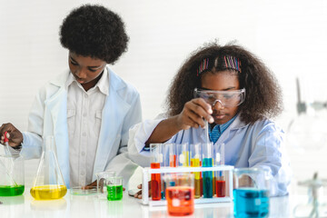 Two african american cute little boy and girl student child learning research and doing a chemical experiment while making analyzing and mixing liquid in test tube at science class on the table