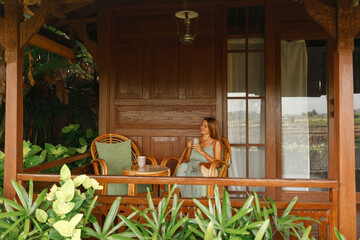 Portrait of a happy smiling caucasian woman, sit on the hotel terrace of wooden housse and drink coffee