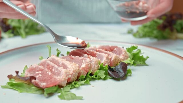 Arranging in a serving plate Seared Tuna with decorative vegetables in 4K. Concept of dressing Tuna and topping up with different spices, coriander, spring onion, red chili, garlic chips.
