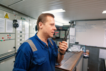 Fototapeta premium Marine Engineer working on radio communication at Engine Control room ECR. Vessel communication with VHF and UHF walkie-talkie radio. Start or stop of main engine