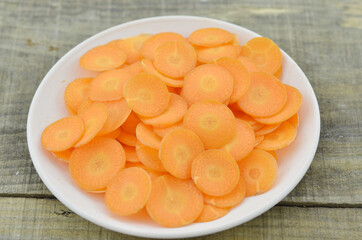 White plate with fresh thin slices carrots on wooden table, closeup