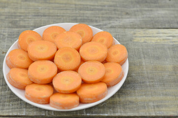 White plate with fresh thick slices carrots on wooden background, closeup