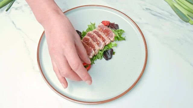 Arranging in a serving plate Seared Tuna with decorative vegetables in 4K. Concept of dressing Tuna and topping up with different spices, coriander, spring onion, red chili, garlic chips.