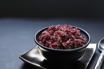 cooked brown rice berry rice (non-glutinous purple rice) in the black bowl on the bamboo mat with chopsticks on the golden ceramic tray on table of the organic food restaurant in Bangkok Thailand