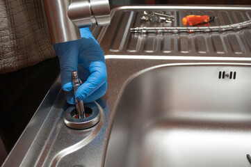 Installation of the water tap to a sink. Hands holds a kitchen faucet with elastic hoses. Repair of a water tap.