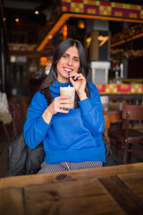 Portrait of pretty brunette in a cafe. Enjoying latte and looking at camera.
