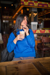 Portrait of pretty brunette in a vintage cafe. Enjoying latte.
