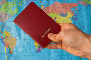 Holding foreign passport against blurred colorful world map background. Time to travel concept