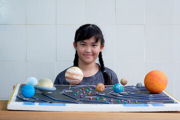 Young smiling Asian girl showing her homemade solar system model for science homework project at schoo