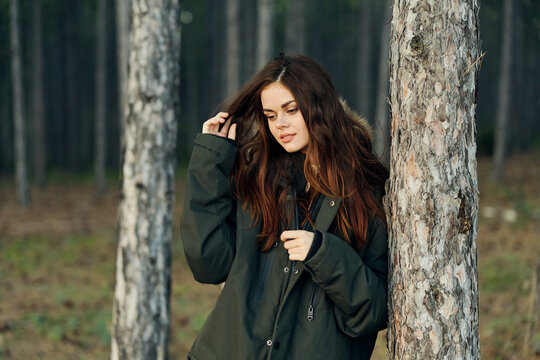 a woman in a black other jacket in the forest holds her hair and looks down