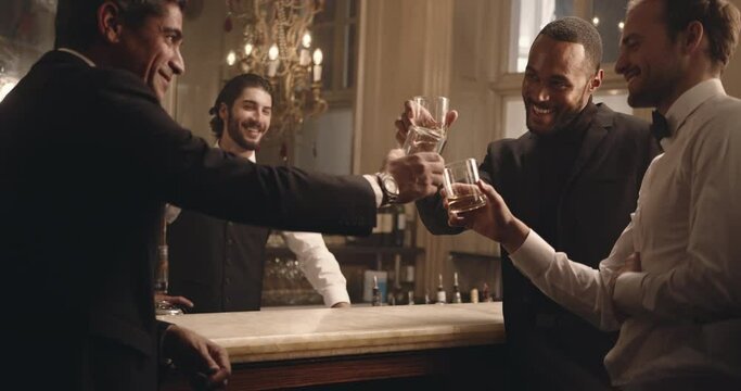 Friends standing at the bar counter and toasting drinks. Group of multi-ethnic men having alcohol at a party. 
