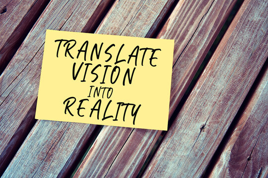 Translate vision into reality. Motivational or inspirational leadership quote on yellow paper on a wooden table.