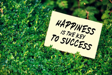 Motivational inspirational quote happiness is the key to success written on paper in a garden with green plants.