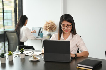 Happy young woman using tablet computer for work in office.