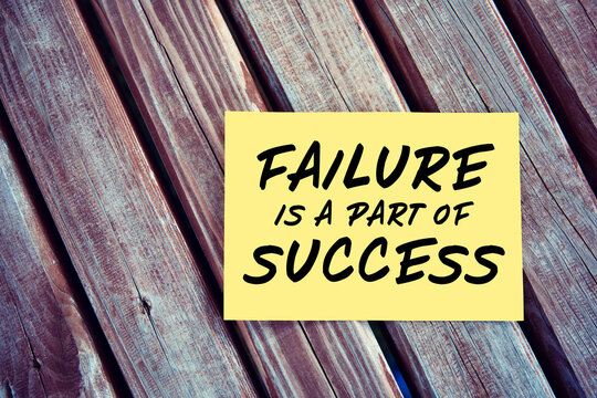 Failure is a part of success inspirational motivational quote written on yellow paper on a wooden table.