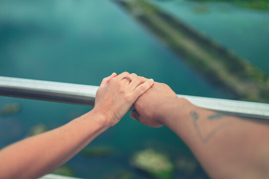 Young couple holding hands on railing by water