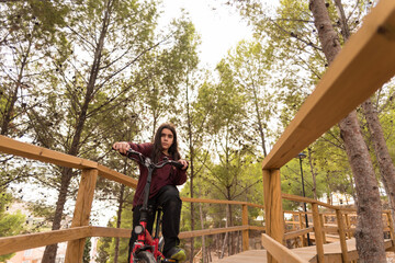 Close-up of a teenager with long hair posing with his bike in a park surrounded by trees and nature.