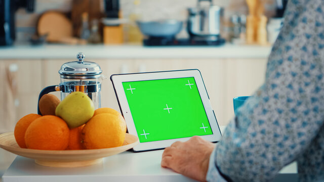 Grandfather looking at tablet pc with green screen during breakfast in kitchen. Elderly person with chroma key isolated mock-up mockup for easy replacement