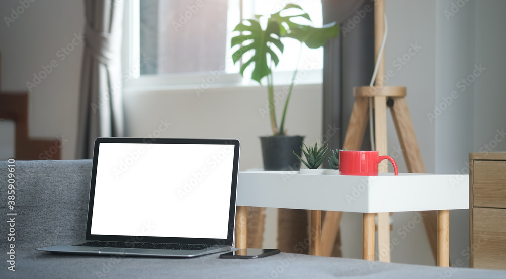 Poster an open laptop computer with blank screen and a smartphone are putting on sofa in living room.