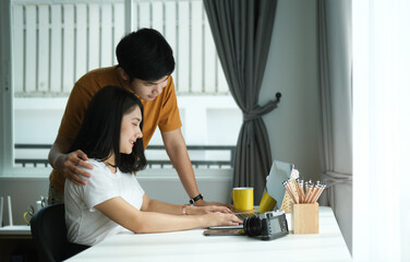 Affectionate young man embracing his wife while looking at computer laptop screen in living room at home.