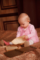 Pretty one-year-old girl in pink dress with an old book is sitting on bed in room. Child in bedroom interior. Concept of education and child rearing. Background for site or banner. Copy space