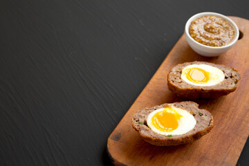 Homemade Scotch Eggs on a rustic wooden board on a black background, side view. Copy space.