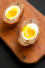 Homemade Scotch Eggs on a rustic wooden board on a black background, side view. Close-up.