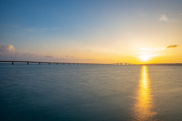 海辺で眺める沈む夕日と橋、宮古島・トゥリバーサンセットビーチ