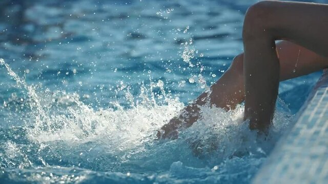 Zappy boy`s legs doing bike movements beat water in a wading pool in slo-mo
