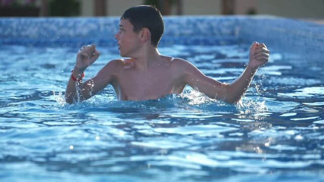 Funny boy jumping and causing many drops in a swimming pool in slow motion
