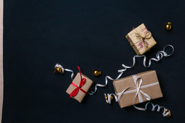 gifts for Christmas, wrapped in wrapping paper and tied with a ribbon, next to the Golden Christmas balls are on a black background. The view from the top. Flatley