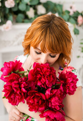Naklejka premium Beautiful red-haired girl holding a bouquet of pink peonies