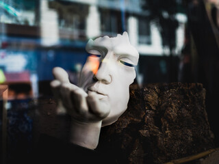 INTERESTING WHITE MASK SCULPTURE AGAINST THE DARK BACK GROUND REFLECTING SURROUNDING AREA