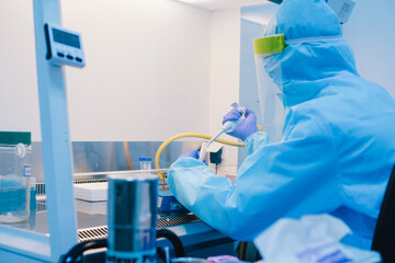 A scientist in PPE safty uniform pipetting sample experiment in biological safety cabinet (BSC).