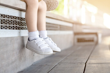 The legs of a boy wearing sneakers. Kid sitting on wooden seat to watch the show. Copy space. © Treechada