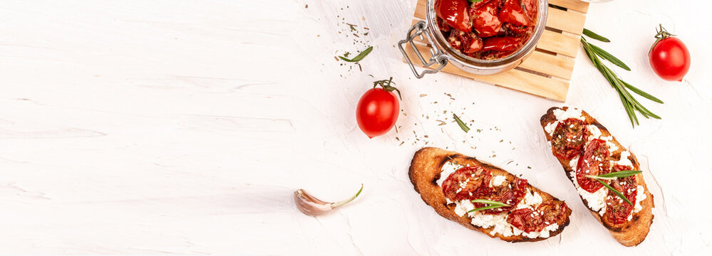sandwich with goat cheese, sun-dried tomatoes and garlic, oregano, olive oil on a light table. space for text. top view. Long banner format