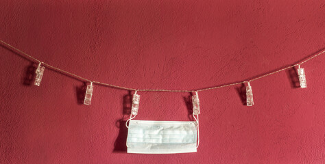 Disinfected pandemic mask drying after washing. Clipped to a string clothesline hanging on a red / magenta wall. New normal concept.