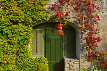 Vieux mur et sa porte en tenue de vigne vierge verte et rouge, Bourgogne-Franche-Comté, France