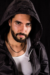 Dramatic portrait of handsome bearded man wearing dark hood looking at camera on a black background