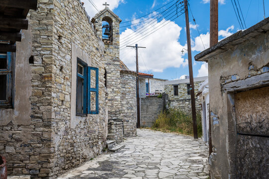 One of the central streets of Kato Lefkara. Very narrow and authentic stony street with wires posts. Cozy houses with colorful facades and red tiled roofs. Chapel with the bell in the middle